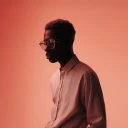 Brown skinned man with glasses wearing brown shirt in brown background.